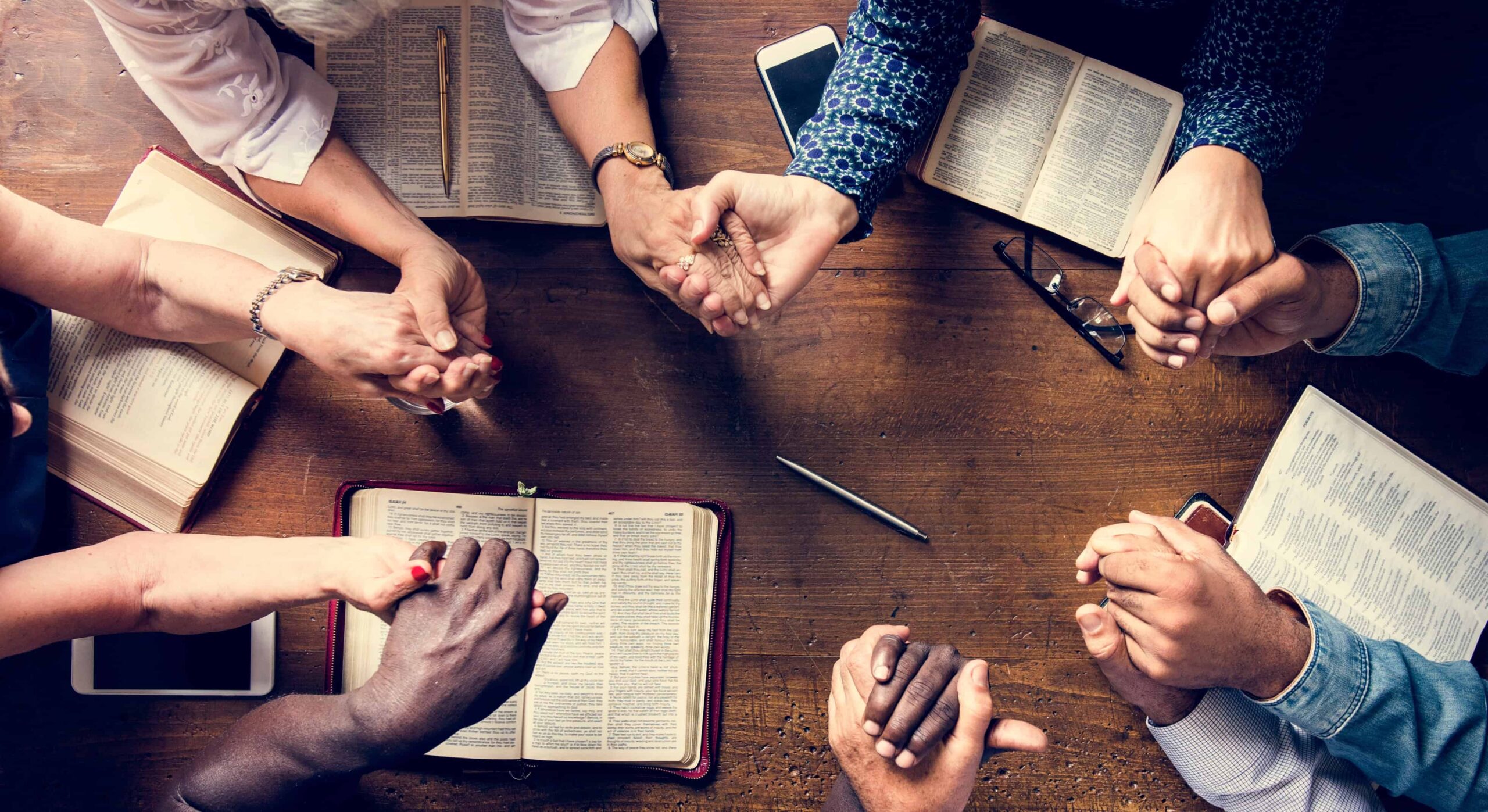 Diverse Group of People Holding Hands in Prayer Around a Table with Open Bibles